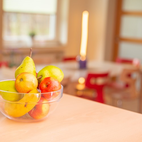 Eine gläserne Obstschale mit Äpfeln, Birnen und Bananen steht auf einem Tisch.